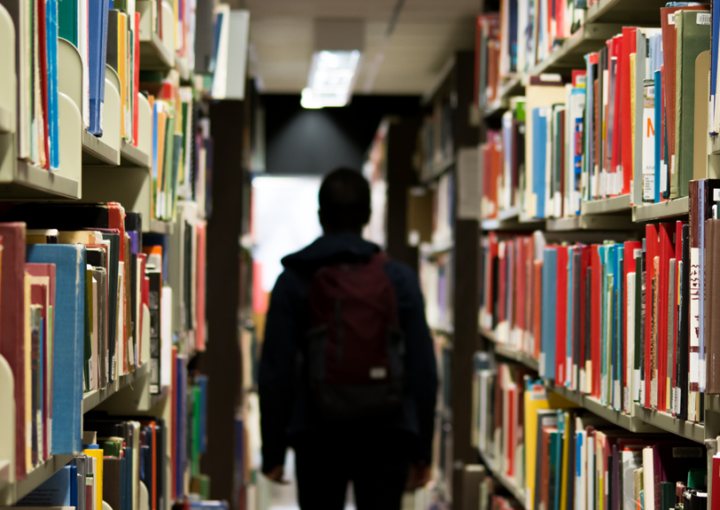 A student walks through rows of books at a library