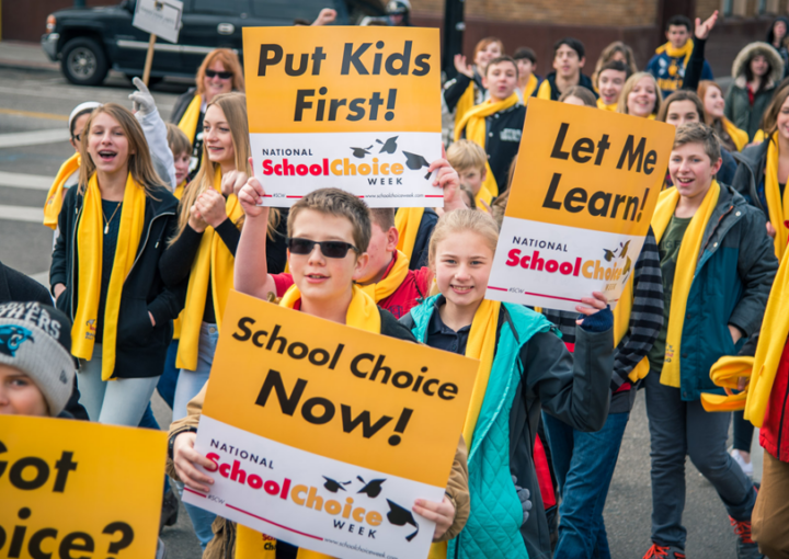 Students hold up signs that say "Put Kids First!" for National School Choice Week